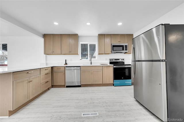 kitchen featuring appliances with stainless steel finishes, sink, light hardwood / wood-style floors, and kitchen peninsula