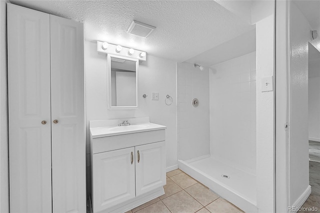 bathroom with vanity, a textured ceiling, tile patterned floors, and tiled shower