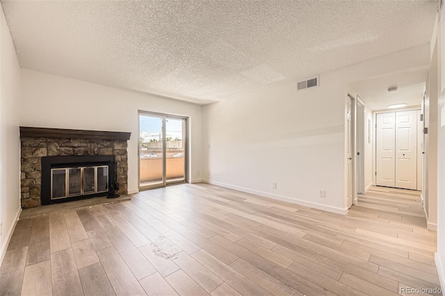 unfurnished living room with light wood-type flooring, baseboards, a textured ceiling, and a stone fireplace