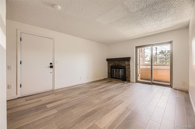 unfurnished living room with light wood-style floors, a textured ceiling, a fireplace, and baseboards