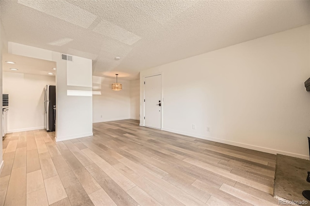 unfurnished room with light wood-style flooring, a chandelier, a textured ceiling, and baseboards