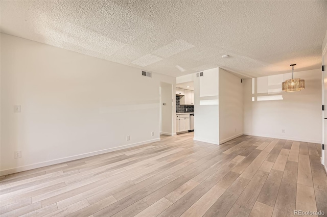 unfurnished living room featuring a textured ceiling, light wood finished floors, baseboards, and a chandelier