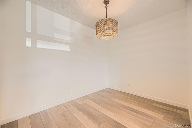 spare room featuring light wood-style flooring, baseboards, and a textured ceiling