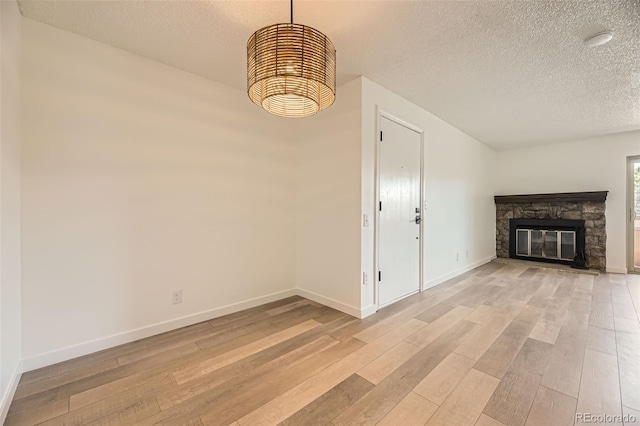 unfurnished living room featuring a textured ceiling, light wood-type flooring, baseboards, and a fireplace