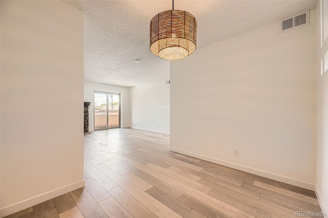 empty room featuring a textured ceiling, baseboards, and light wood finished floors