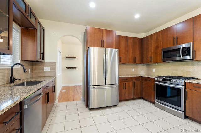 kitchen featuring tasteful backsplash, light stone counters, sink, and appliances with stainless steel finishes