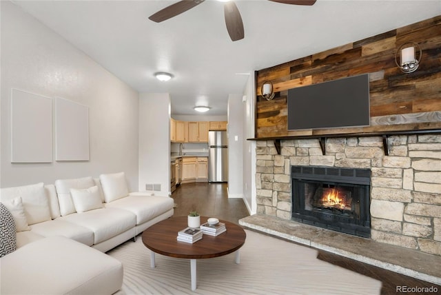 living room with a fireplace, baseboards, visible vents, ceiling fan, and dark wood-type flooring