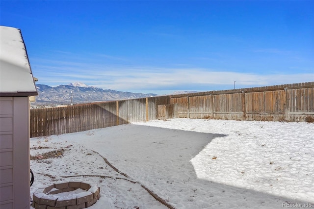 yard layered in snow with a mountain view and a fire pit