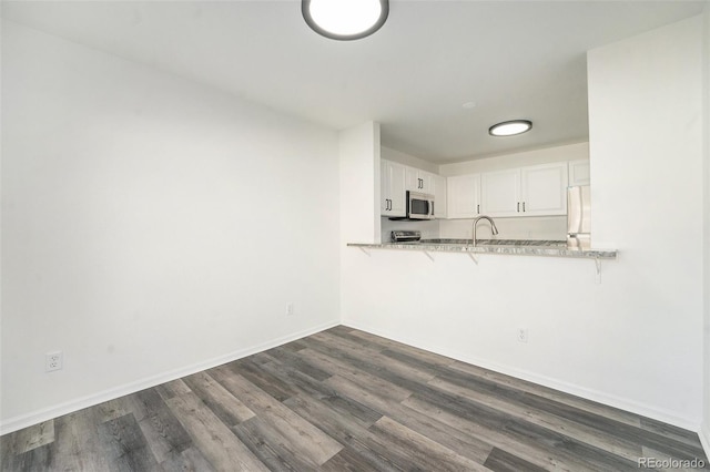 kitchen featuring white refrigerator, kitchen peninsula, light stone counters, dark hardwood / wood-style flooring, and white cabinetry