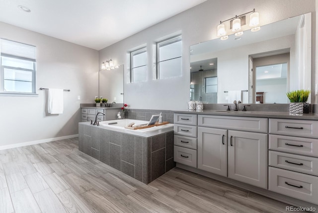 full bathroom with vanity, a garden tub, plenty of natural light, and baseboards