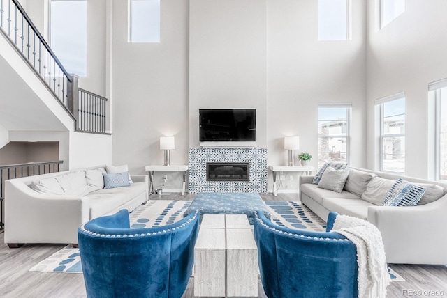 living area with a tiled fireplace, a towering ceiling, and wood finished floors