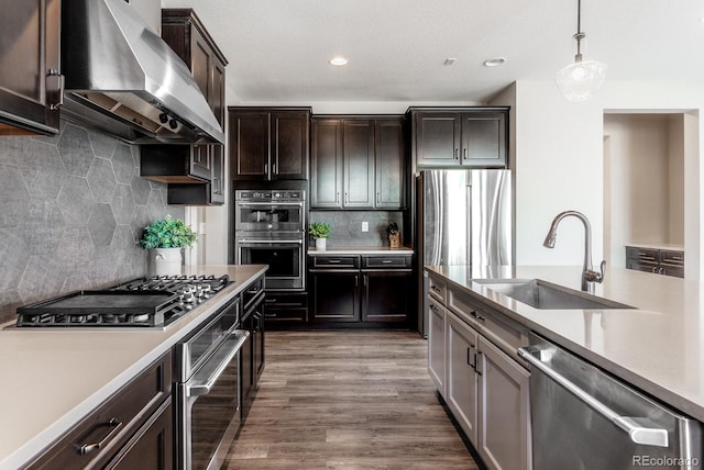 kitchen with dark wood-style floors, a sink, light countertops, appliances with stainless steel finishes, and wall chimney range hood