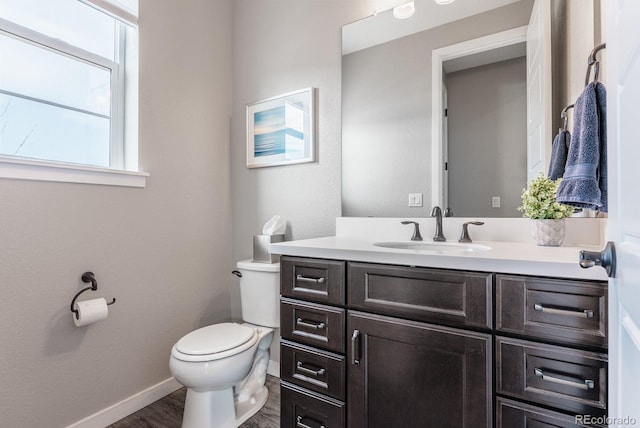 bathroom featuring baseboards, toilet, wood finished floors, and vanity