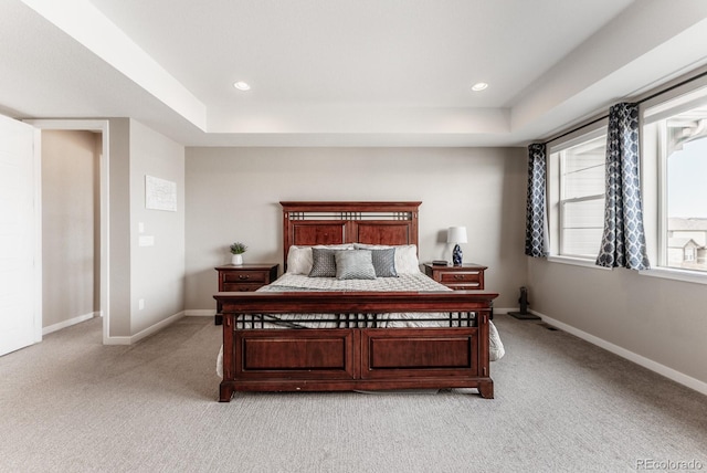 bedroom with a raised ceiling, recessed lighting, light colored carpet, and baseboards