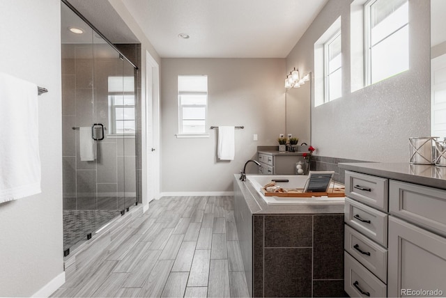 full bathroom with vanity, baseboards, wood finish floors, a stall shower, and a relaxing tiled tub