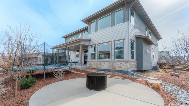 back of house with cooling unit, stone siding, a trampoline, and a patio