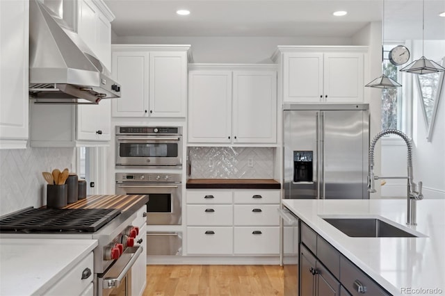 kitchen featuring tasteful backsplash, high end appliances, wall chimney range hood, white cabinets, and hanging light fixtures