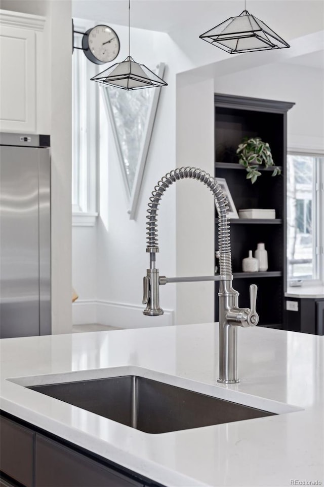 details featuring white cabinets, decorative light fixtures, sink, and stainless steel refrigerator