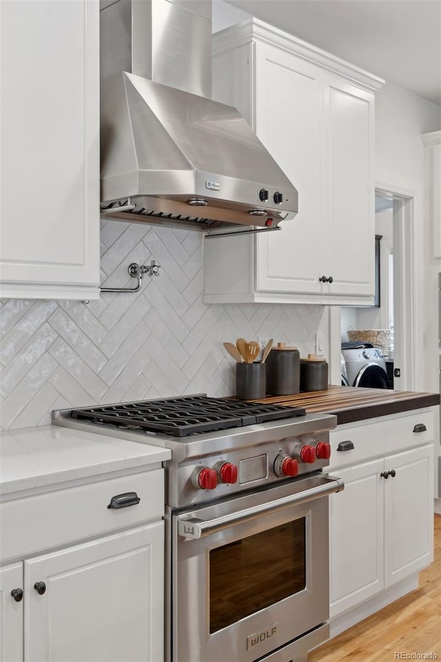 kitchen with wall chimney exhaust hood, designer range, decorative backsplash, light wood-type flooring, and white cabinetry