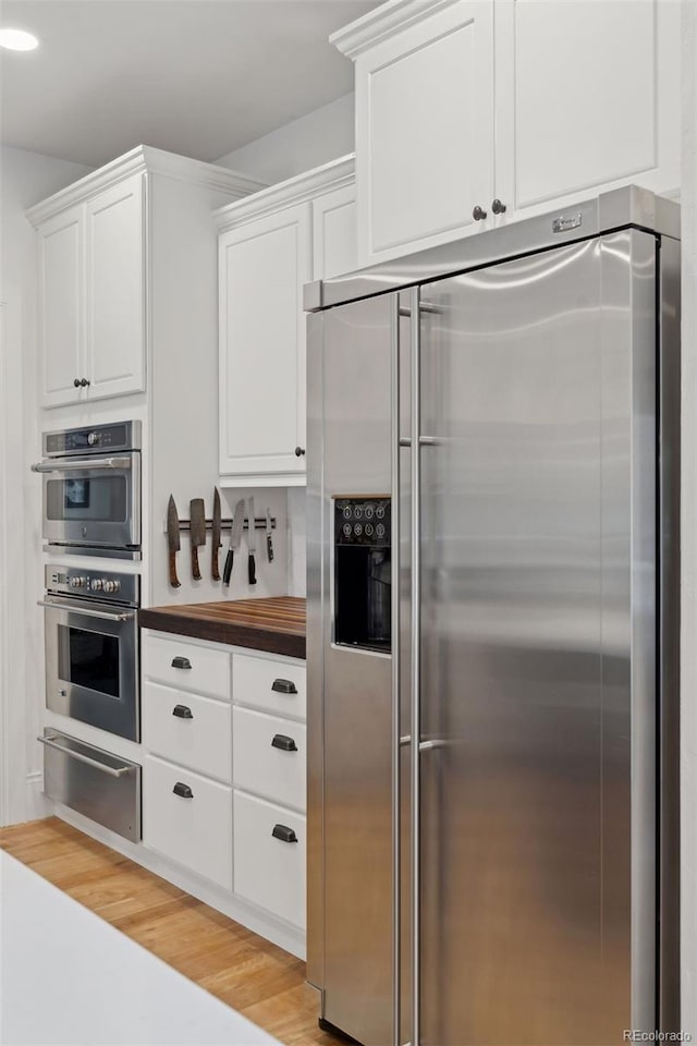 kitchen featuring white cabinets, wooden counters, appliances with stainless steel finishes, and light hardwood / wood-style flooring