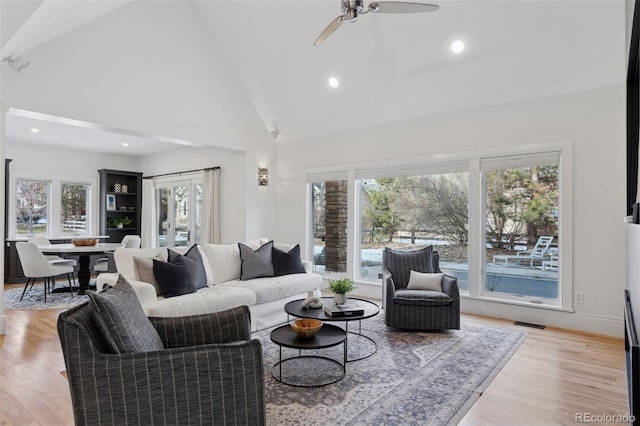 living room featuring ceiling fan, light hardwood / wood-style flooring, high vaulted ceiling, and a healthy amount of sunlight