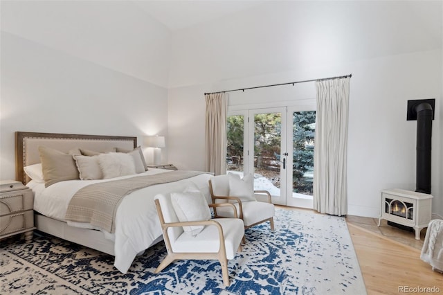 bedroom featuring access to exterior, french doors, wood-type flooring, high vaulted ceiling, and a wood stove