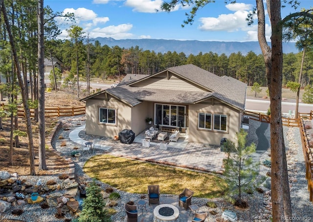 rear view of house featuring an outdoor fire pit, roof with shingles, a patio area, and a view of trees