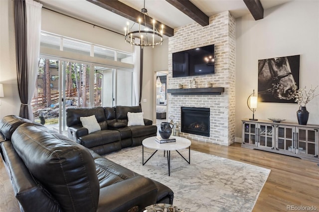 living room with a chandelier, wood finished floors, beamed ceiling, a fireplace, and a towering ceiling