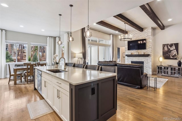 kitchen featuring a sink, white cabinetry, a fireplace, light wood finished floors, and dishwasher