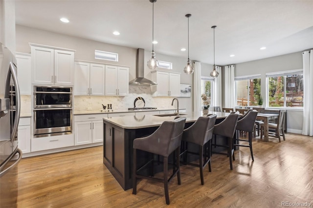 kitchen with wall chimney exhaust hood, a sink, a kitchen breakfast bar, appliances with stainless steel finishes, and backsplash