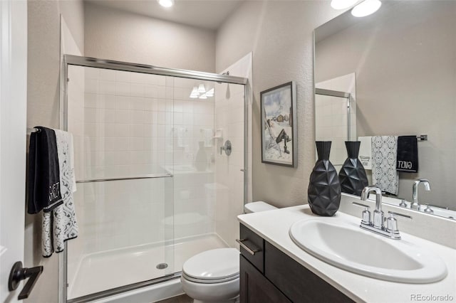 full bathroom featuring a textured wall, toilet, a shower stall, and vanity