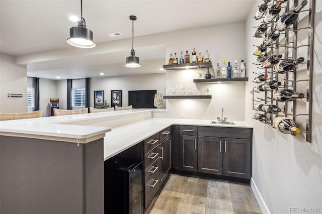 kitchen featuring a sink, light wood-type flooring, hanging light fixtures, light countertops, and a peninsula