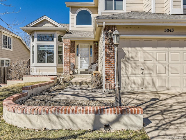 entrance to property featuring a garage, driveway, roof with shingles, and brick siding