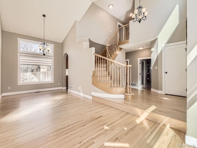 foyer featuring a towering ceiling, stairs, a chandelier, and wood finished floors