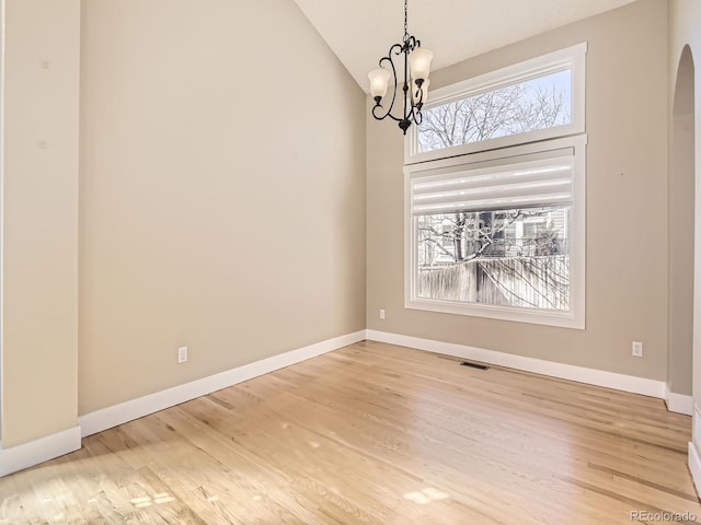 unfurnished dining area featuring arched walkways, wood finished floors, visible vents, and baseboards