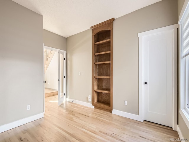 unfurnished bedroom featuring a textured ceiling, light wood finished floors, and baseboards