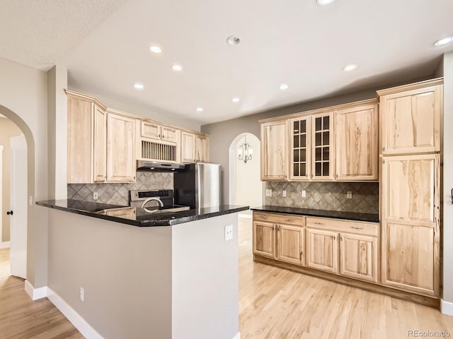 kitchen featuring arched walkways, under cabinet range hood, light wood-type flooring, freestanding refrigerator, and light brown cabinetry