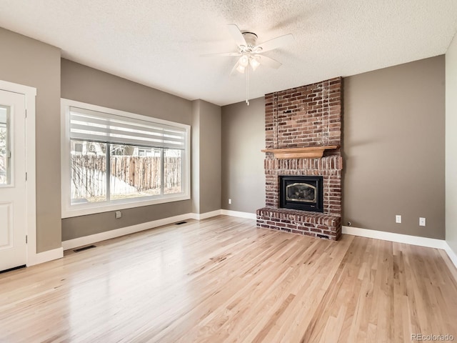 unfurnished living room with a brick fireplace, a textured ceiling, visible vents, and wood finished floors