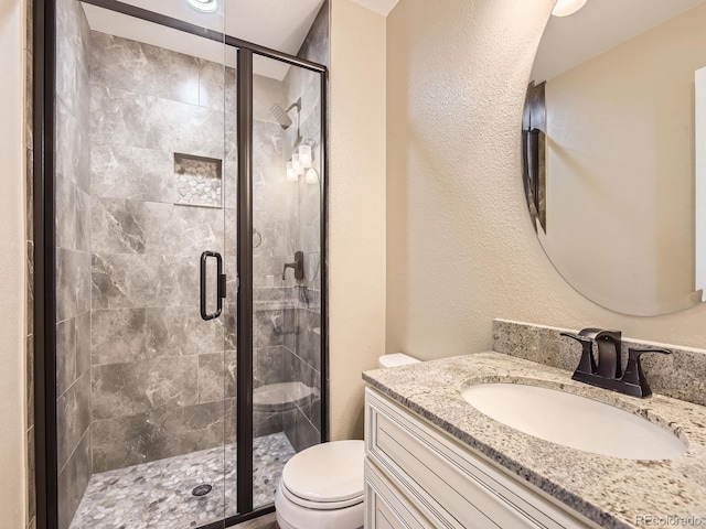 full bathroom featuring toilet, a stall shower, a textured wall, and vanity