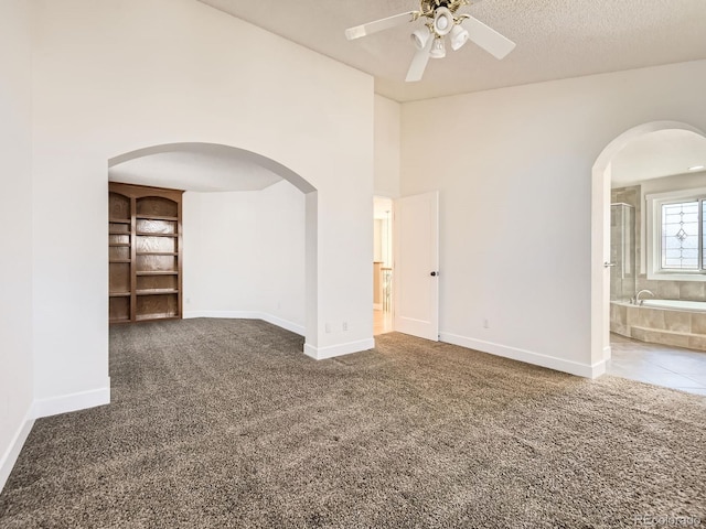 carpeted spare room featuring baseboards, arched walkways, ceiling fan, a high ceiling, and a textured ceiling