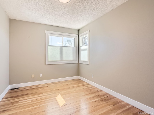 empty room with visible vents, light wood-style flooring, baseboards, and a textured ceiling