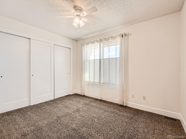 unfurnished bedroom featuring a closet, visible vents, dark carpet, a textured ceiling, and baseboards