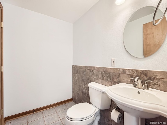 bathroom featuring baseboards, toilet, a sink, tile patterned flooring, and tile walls