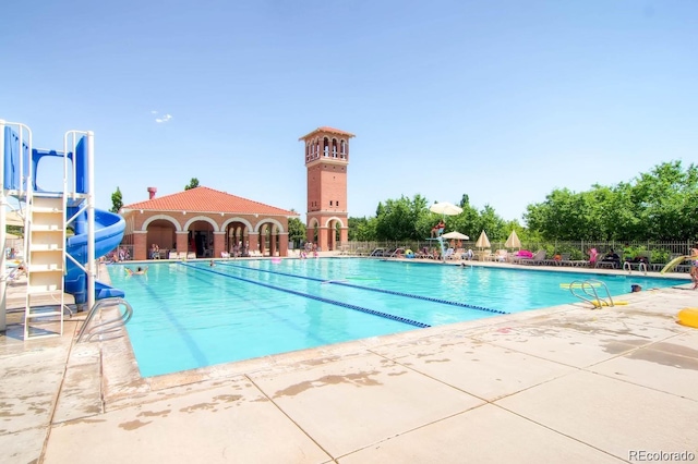 community pool featuring a water slide, a patio area, fence, and a water play area