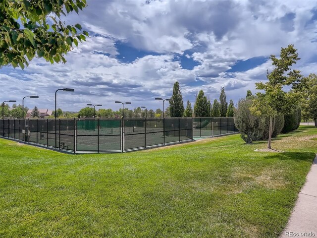 view of tennis court with fence and a lawn