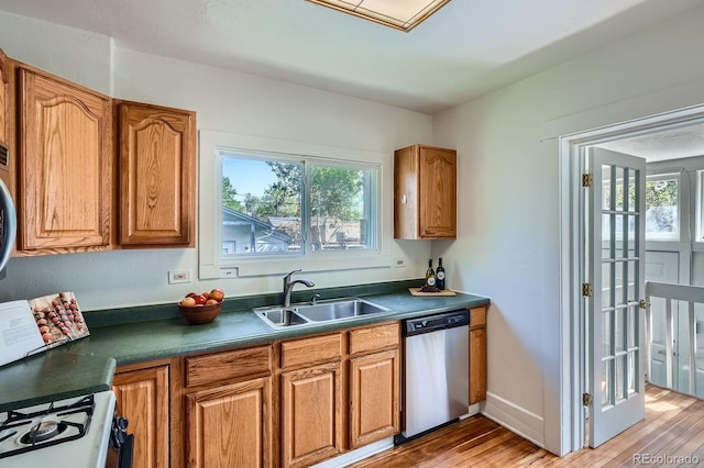 kitchen with stainless steel dishwasher, a sink, dark countertops, and plenty of natural light
