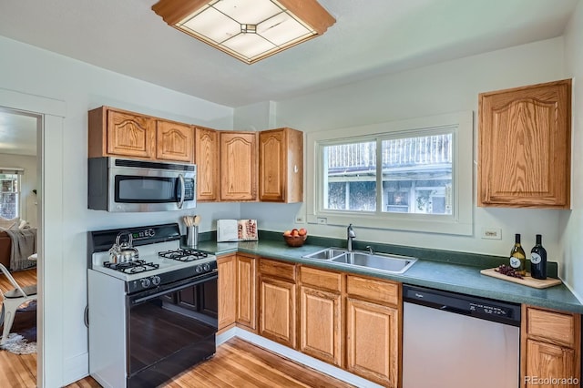 kitchen with stainless steel appliances, a sink, light wood-type flooring, and dark countertops