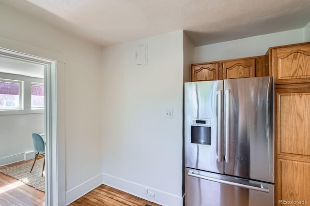 kitchen featuring stainless steel fridge, light wood-style flooring, baseboards, and brown cabinets