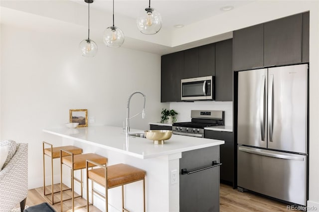 kitchen featuring dark cabinets, stainless steel appliances, a peninsula, a kitchen breakfast bar, and light wood-type flooring