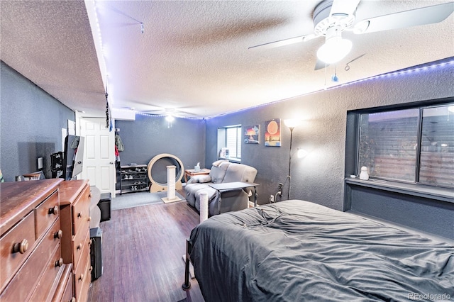 bedroom featuring ceiling fan, wood finished floors, a textured wall, and a textured ceiling